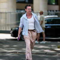 Alex Badia wears silver metallic sunglasses, dark brown beaded necklaces, white tank top, light blue unbuttoned long sleeve shirt, shiny dark brown...