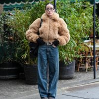 Alexandra Guerain wears black glasses, silver hoop earrings, light brown faux fur zipped cropped jacket, black long sleeve shirt, shiny black leather...