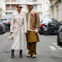 Alice Barbier wears black sunglasses, a beige suede shoulder-pads / belted long coat, a beige and white shiny leather handbag, black shiny leather...