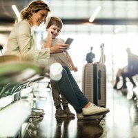 alleinerziehende mutter und sohn benutzen handy, während sie auf ihren transport im abflugbereich warten. - travel stock-fotos und bilder