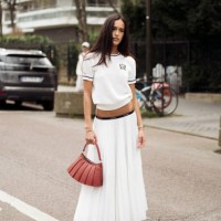 Amalie Bladt wears white maxi pleated skirt, white short sleeve top and red bag outside the Lacoste fashion show during the Womenswear Fall/Winter...