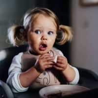 amazed cute toddler girl with pigtails eating at a table at home. - food stock pictures, royalty-free photos & images