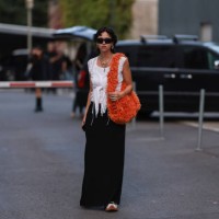 Amelie Kahl is seen wearing black shades, silver earrings and necklaces, white top, fluffy orange Miu Miu shoulder bag, black long skirt and black...