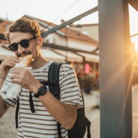 an adult fashionable man is walking in the city and eating a sandwich - junk food stock pictures, royalty-free photos & images