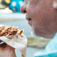 an adult man eating a sandwich on the street. - junk food stock pictures, royalty-free photos & images