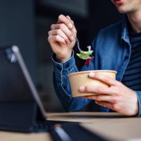 an anonymous student studying online on his digital tablet and eating lunch in the library - junk food stock pictures, royalty-free photos & images
