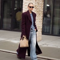 Andrea Steen wears blue jeans, burgundy coat, blue sweater and beige bag outside the Herskind fashion show during the Copenhagen Fashion Week...