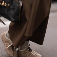 Anna Wein is seen wearing an ankle-length brown wool trench coat from Sandro, a rectangular black leather bag with gold details from Miu Miu, beige...