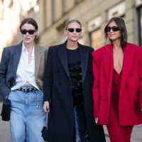 Annabel Rosendahl wears a white shirt, a bicolored gray and brown blazer jacket, a black shiny leather nailed / studded belt, a pale blue faded denim...