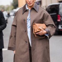 Ashley Graham, wearing a brown trench coat and trousers, a light blue and white striped shirt and and light brown leather bag, is seen outside Tod's...