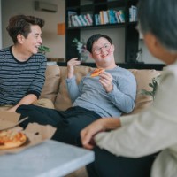 asian chinese multi generation family with down syndrome grandson enjoying pizza fast food in living room sitting on sofa during weekend - junk food stock pictures, royalty-free photos & images