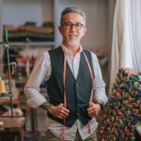 asian chinese senior tailor man with facial hair looking at camera smiling in atelier studio - fashion stock pictures, royalty-free photos & images