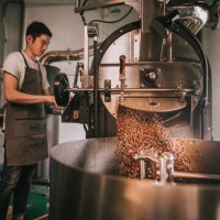 asian craftsperson observing freshly roasted coffee beans being removed from the roaster into the cooling cylinder with motion blur dropping point - coffee stock pictures, royalty-free photos & images