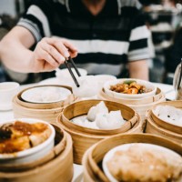 asian man picking up siu mai with chopsticks and enjoying a variety of freshly made dim sum in restaurant - junk food stockfoto's en -beelden