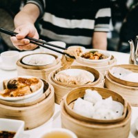 asian man picking up steamed beancurd roll with chopsticks and enjoying a variety of dim sum in restaurant - junk food stockfoto's en -beelden