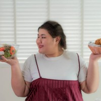 asian overweight woman holding salad in right hand and fries chicken in left hand, choosing healthy or unhealthy food nutrition . she looking happy to eat salad. concept of eating healthy or unhealthy lifestyle. - junk food s