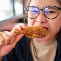 asian woman biting a pieces of fried chicken. - junk food stock pictures, royalty-free photos & images