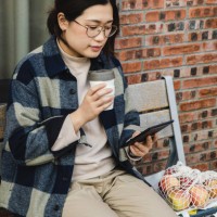 asian woman reading an e-book while drinking coffee using a reusable cup - junk food stock pictures, royalty-free photos & images