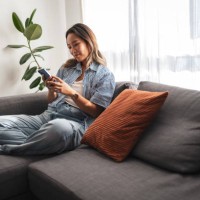 asian woman relaxing on a comfortable sofa with a smartphone - home decoration stock pictures, royalty-free photos & images