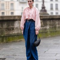 Astrid Boutrot wears gold earrings, light pink long sleeve shirt, navy blue high waisted denim jean pants, black Alaïa leather bag, shiny dark brown...