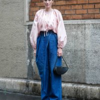 Astrid Boutrot wears silver earrings, light pink long sleeve oversized shirt, navy blue denim jean baggy pants, black Alaïa leather bag, shiny black...
