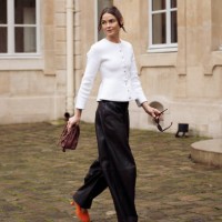 Bambi Northwood-Blyth wears black leather pants, white jacket with buttons, orange high heels and brown Loewe bag outside the Loewe presentation...