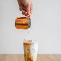 barista hand pouring milk into an iced coffee for making iced latte. - coffee stockfoto's en -beelden