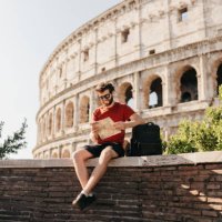 bearded male tourist reading map and smiling with colosseum in background - travel stock pictures, royalty-free photos & images