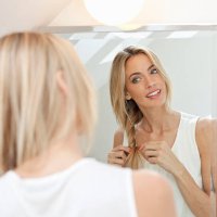 beautiful blonde doing her hair in front of mirror - hairstyle stock pictures, royalty-free photos & images