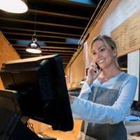 beautiful saleswoman registering a takeout order while talking with the customer on a smartphone looking happy - junk food stock pictures, royalty-free photos & images