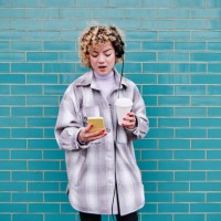 beautiful woman with coffee cup listening music through headphones while using smart phone against blue wall - junk food stock pictures, royalty-free photos & images
