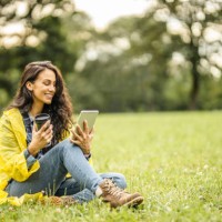 beautiful young lady in yellow raincoat reading a book on her digital tablet, drinking tea and sitting on grass while taking a break in nature - junk food stock pictures, royalty-free photos & images