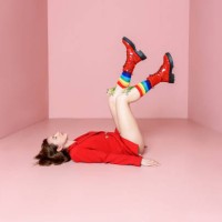 beautiful young woman in a red jacket posing while lying on a pink background in colored rainbow socks from which flowers grow and boots. fashion concept. - fashion stock pictures, royalty-free photos & images