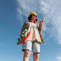 beautiful young woman in summer clothes using smart phone and holding skateboard on blue sky background. internet concept - fashion stock pictures, royalty-free photos & images