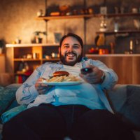 übergewichtiger mann essen fast food und vor dem fernseher - junk food stock-fotos und bilder