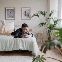 black woman writing in a notebook while laying on a comfortable bed at home. - home decoration stock pictures, royalty-free photos & images