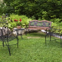 black wrought iron antique style armchairs and sitting bench painted brownish orange and red super moon red geraniums (pelargonium hortorum) in flower pot on table in front yard garden in summer, quebec, canada. this image is