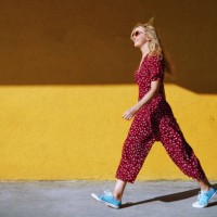 blond woman wearing burgundy jumpsuit and sunglasses while walking against the yellow wall - fashion photos et images de collection