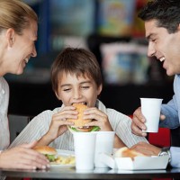 boy eating hamburger in fast food restaurant with his parents - junk food stock pictures, royalty-free photos & images