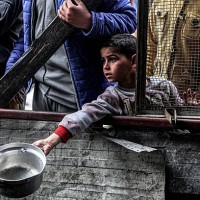 Boy holds out an empty pot as he waits with other displaced Palestinians queueing for meals provided by a charity organisation ahead of the...