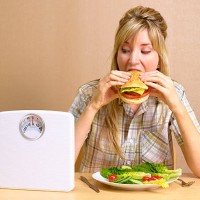 bulimic girl eating burger with bathroom scales - junk food stock pictures, royalty-free photos & images