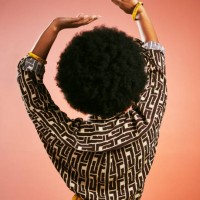 carefree fashionable retro woman dancing listening to music and having fun. portrait from behind of a funky and stylish female with afro hair isolated on a brown background. - fashion stock pictures, royalty-free photos & ima