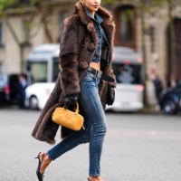 Caroline Daur wears silver earrings, black bandeau top, navy blue denim jean cropped jacket, black belt, washed navy blue denim jean skinny pants,...