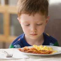 caucasian boy looking at plate of eggs and bacon - food stockfoto's en -beelden