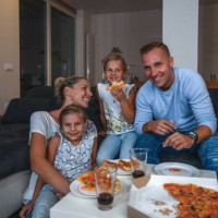 caucasian family sitting on a sofa eating pizza and watching tv - junk food stock pictures, royalty-free photos & images