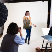 caucasian female photographer, taking photos of the female fashion model black ethnicity, while posing with an leather bag - fashion stock pictures, royalty-free photos & images