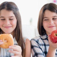 caucasian twin sisters eating healthy and unhealthy snacks - junk food stock pictures, royalty-free photos & images