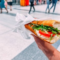 caucasian young man's hand holding a caprese italian sandwich while on the go in a busy crowded train station in london, uk - junk food stock pictures, royalty-free photos & images
