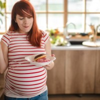 charming pregnant woman holding a plate with donughts and enjoyig her cravings - junk food stock pictures, royalty-free photos & images
