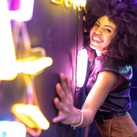 cheerful afro american woman with afro hair leaning with her hands on a wall with neon signs looking at the camera - fashion stock pictures, royalty-free photos & images